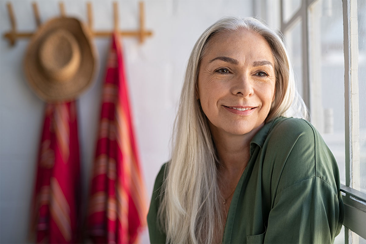 a woman leaning against a window and smiling after getting a primary facelift in Raleigh at Stein Plastic Surgery