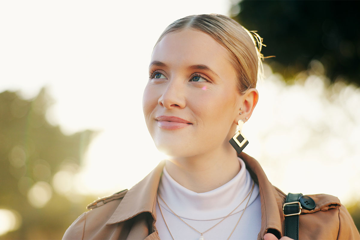a woman smiling outdoors in the sun after getting a rhinoplasty by expert rhinoplasty surgeon in Raleigh, Dr. Stein