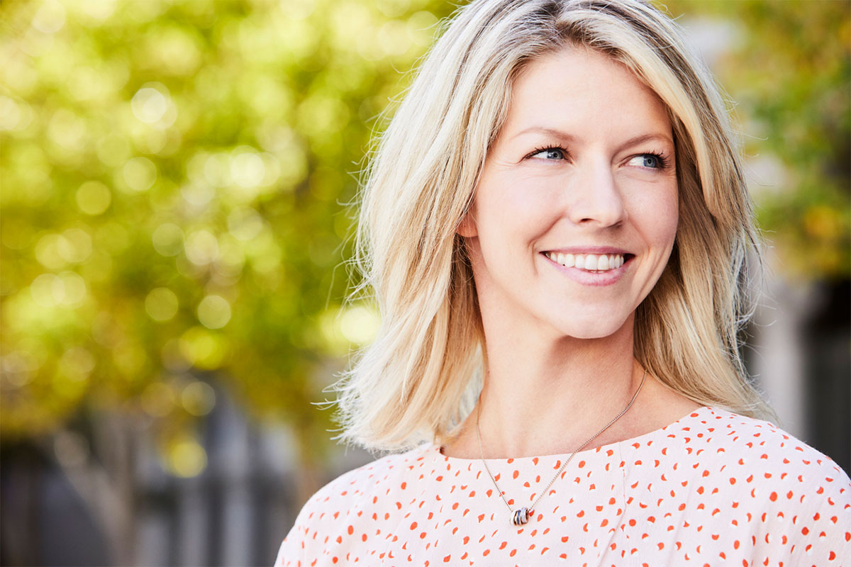 a woman standing outside smiling after getting open rhinoplasty in Raleigh, NC at Stein Plastic Surgery
